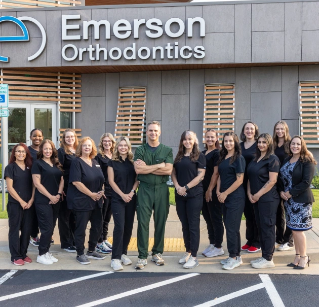 Emerson Orthodontics team members in black scrubs standing together outside clinic building.