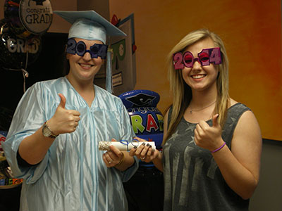 Two people wearing novelty sunglasses give thumbs up gestures indoors at an orthodontics office event.