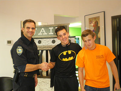 Police officer and two young boys in orthodontics office setting, shaking hands and smiling.