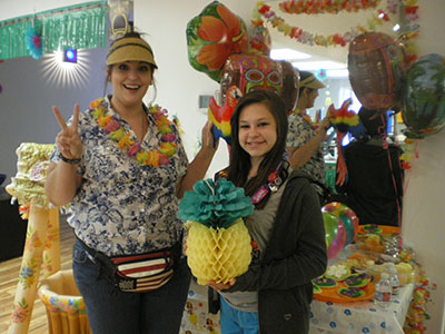 Two people in tropical-themed costumes holding decorative pineapple props in festive office setting.