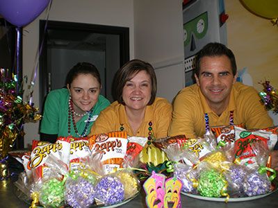 Three smiling staff members display colorful holiday floral arrangements at Emerson Orthodontics office party.