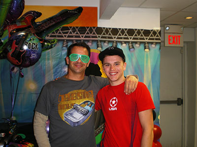 Two people posing together in an office setting wearing colorful sunglasses and festive attire.