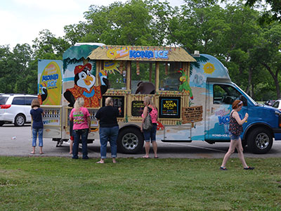 Children gather around colorful food truck in grassy park setting during sunny day.