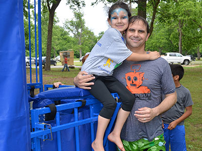 Father holding young child on blue outdoor equipment at park or outdoor event.
