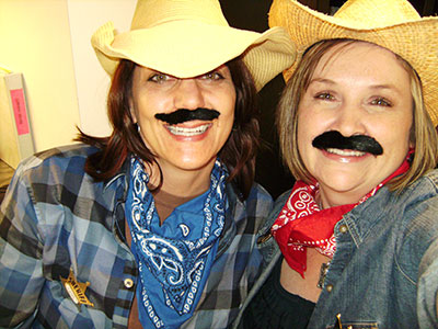 Two people wearing cowboy hats and fake mustaches at an orthodontics office event or party.