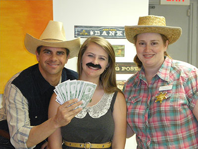 Three people in cowboy hats posing with play money at Emerson Orthodontics office event.