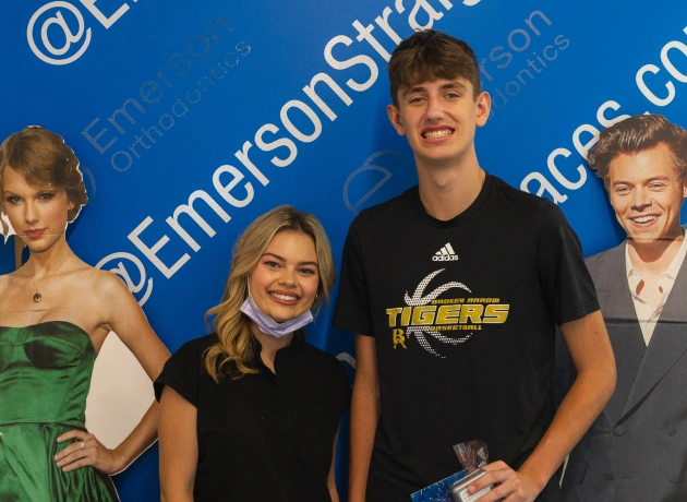 Four young people posing together at Emerson Orthodontics event with blue branded backdrop.