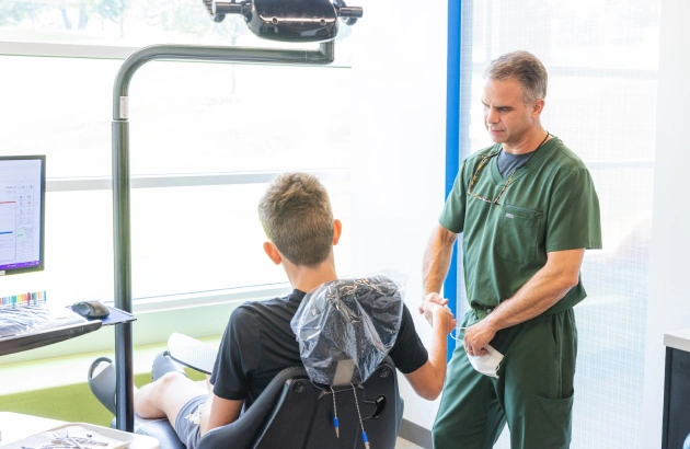 Orthodontist in green scrubs examines young patient's teeth during dental appointment in modern clinic.