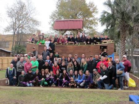 Large group of people posing together on wooden playground structure in outdoor community setting.