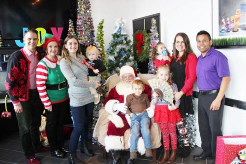 Large group of people and children in holiday attire posing together in decorated Christmas setting indoors.