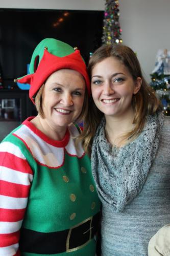 Two women smiling at camera during holiday celebration with Christmas decorations visible in background.