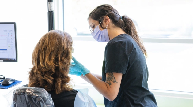 Orthodontist examining patient's teeth in bright clinical office setting with computer monitor visible.