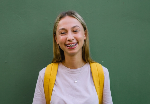 Smiling young woman in yellow cardigan against green wall backdrop