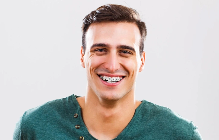 Young man smiling at camera wearing teal v-neck shirt against white background.