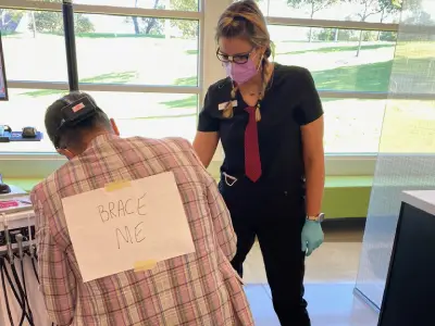 Orthodontist examining patient's back wearing plaid shirt in clinical office setting.