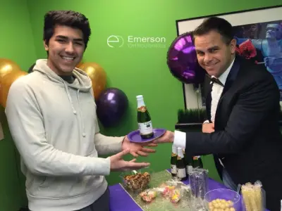 Two men exchange a purple award or trophy at Emerson Orthodontics event with green backdrop.