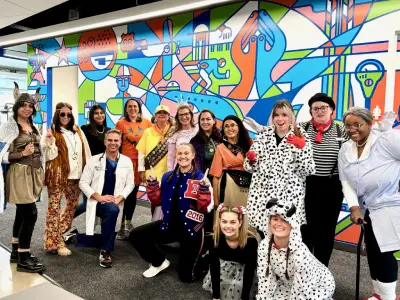 Large group of people posing together in front of colorful abstract mural artwork indoors.