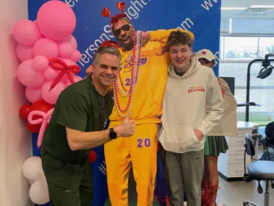Two men pose with mascot character in yellow jersey at orthodontics office event with pink balloons.