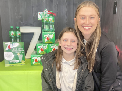 Two smiling people pose together at an orthodontics event with branded product display.