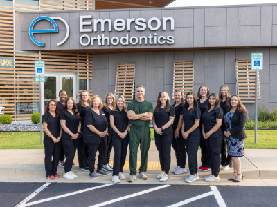 Emerson Orthodontics team standing together outside their office building in matching dark uniforms.