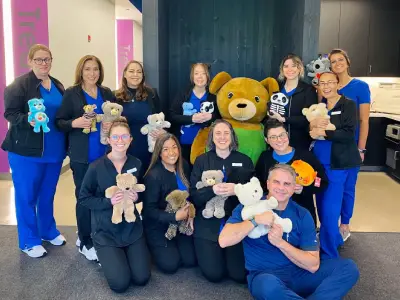 Emerson Orthodontics team members holding stuffed animals in blue scrubs, posing together indoors.
