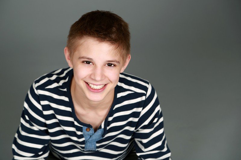 Smiling young boy wearing striped shirt against neutral gray background studio portrait.