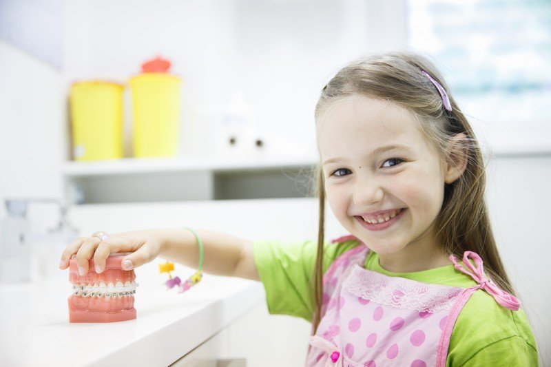 Young girl smiling while placing item in white container in bright, modern kitchen setting.