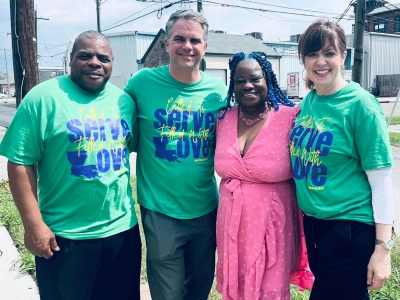Four people wearing green charity event shirts pose together outdoors at Emerson Orthodontics.