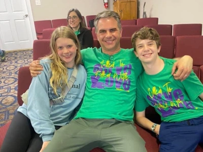 Four people smiling at camera in casual indoor setting, two wearing matching green shirts.