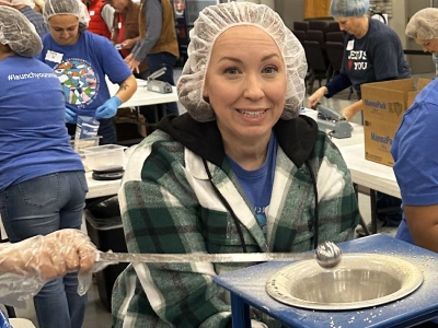 Woman in hairnet and plaid shirt serving food at community event indoors.