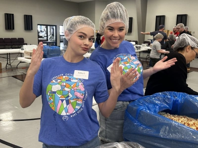 Two people wearing hairnets and blue shirts holding food items at a community event or food service gathering.