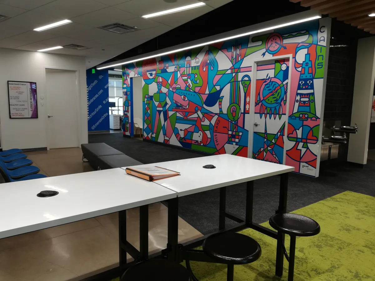 Modern orthodontics office break room with white desk, colorful mural, and green carpet flooring.