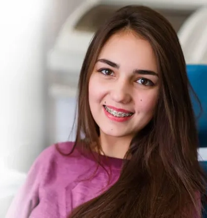 Young woman smiling at camera wearing pink shirt in bright orthodontic office setting.