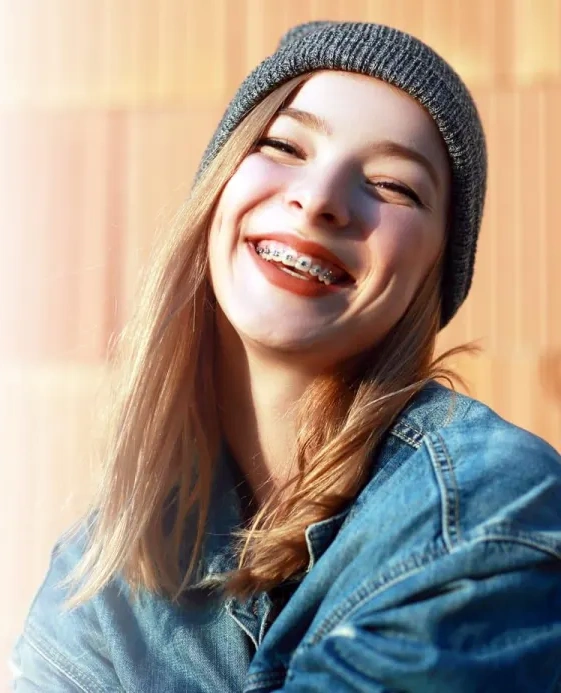 Young woman smiling brightly while wearing denim jacket and gray beanie outdoors.