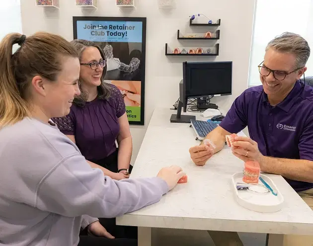 Dental team member showing retainer club information to patient at consultation desk.