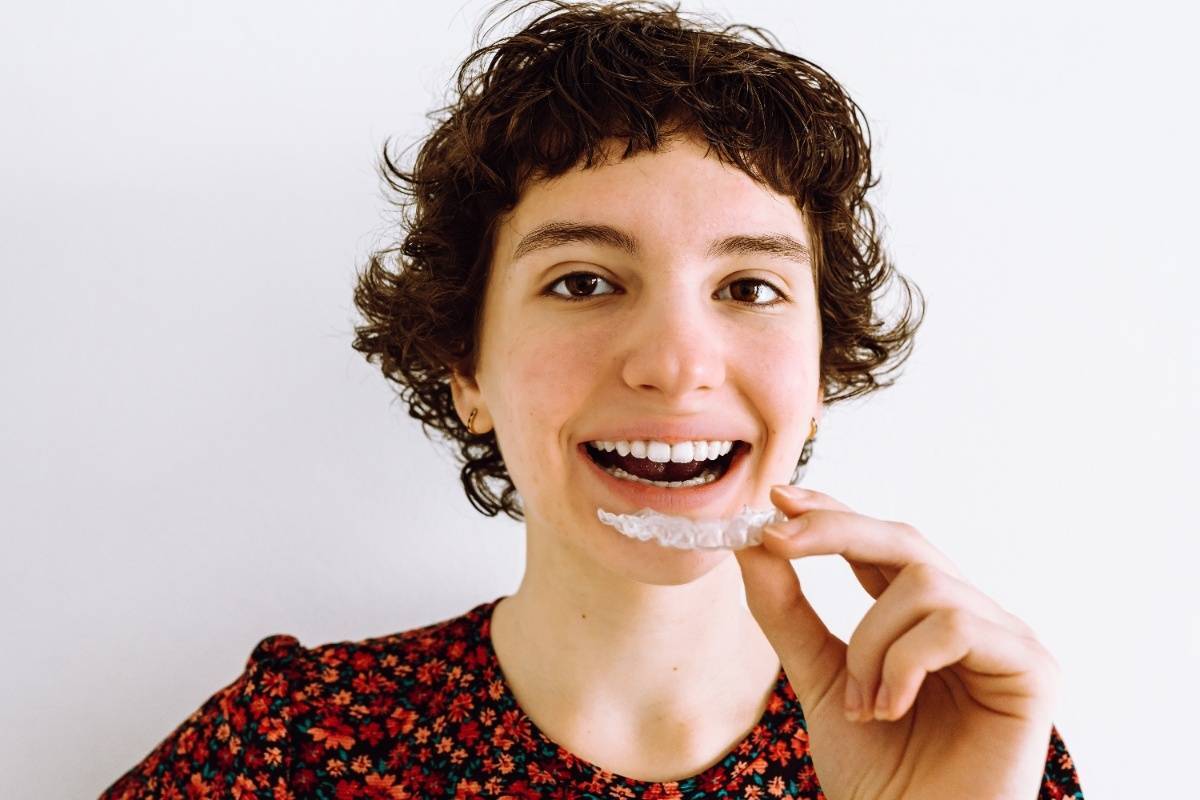 Happy patient holding clear Invisalign aligner tray while smiling in Broken Arrow dental office.