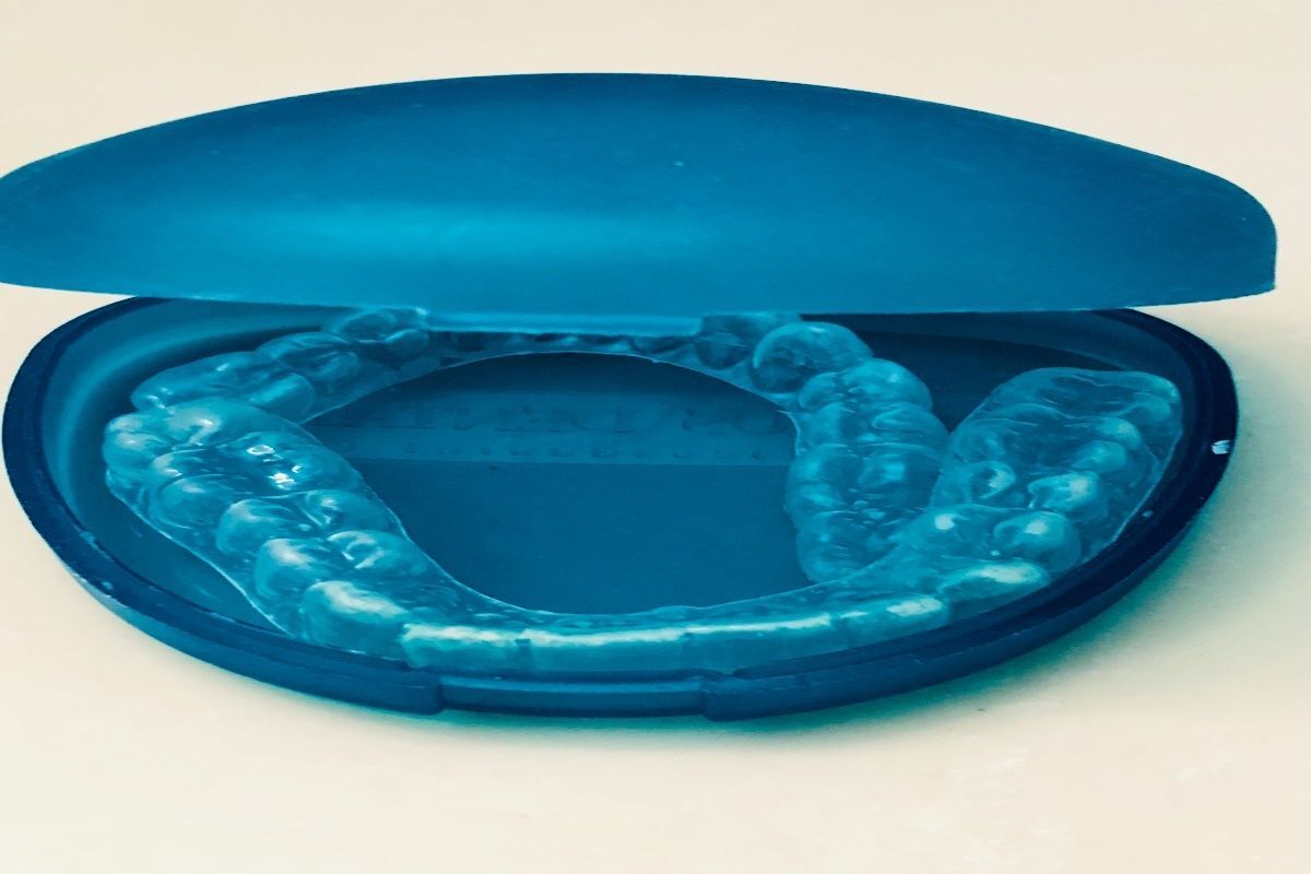 Open blue dental retainer case displaying clear aligners inside.